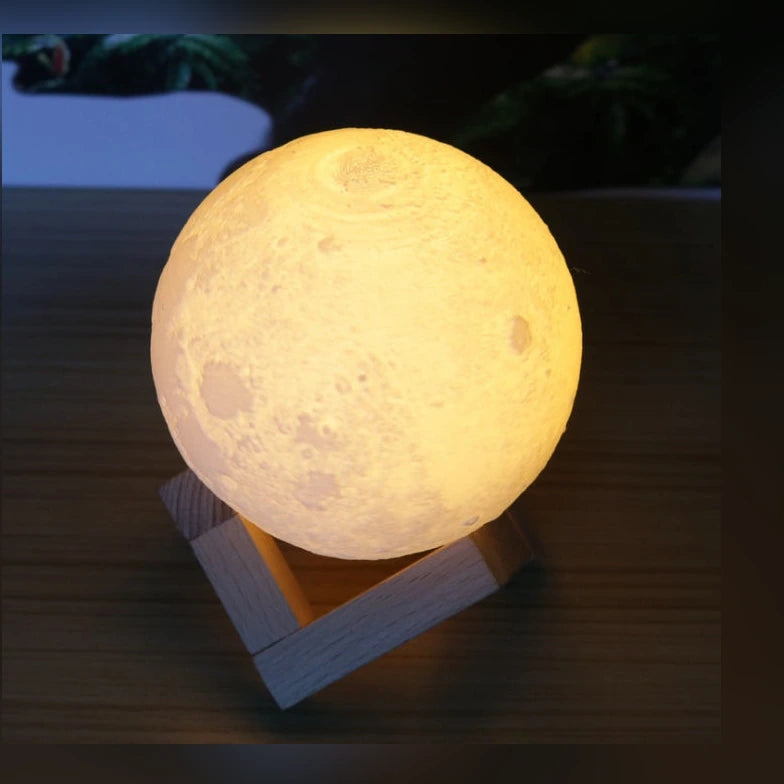 The Mourning Moon lunar glow lamp, lit warm amber, resting on its included wooden stand