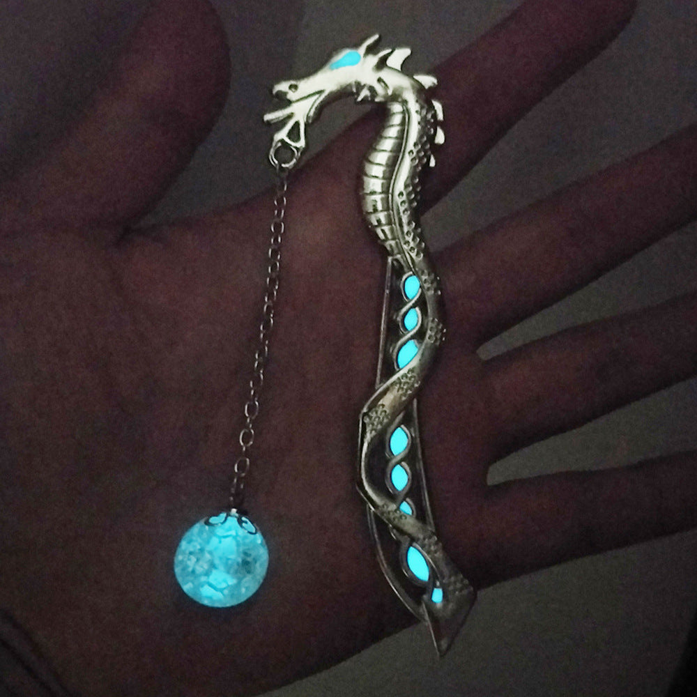 Bronze dragon bookmark with glowing pendant bead in low light