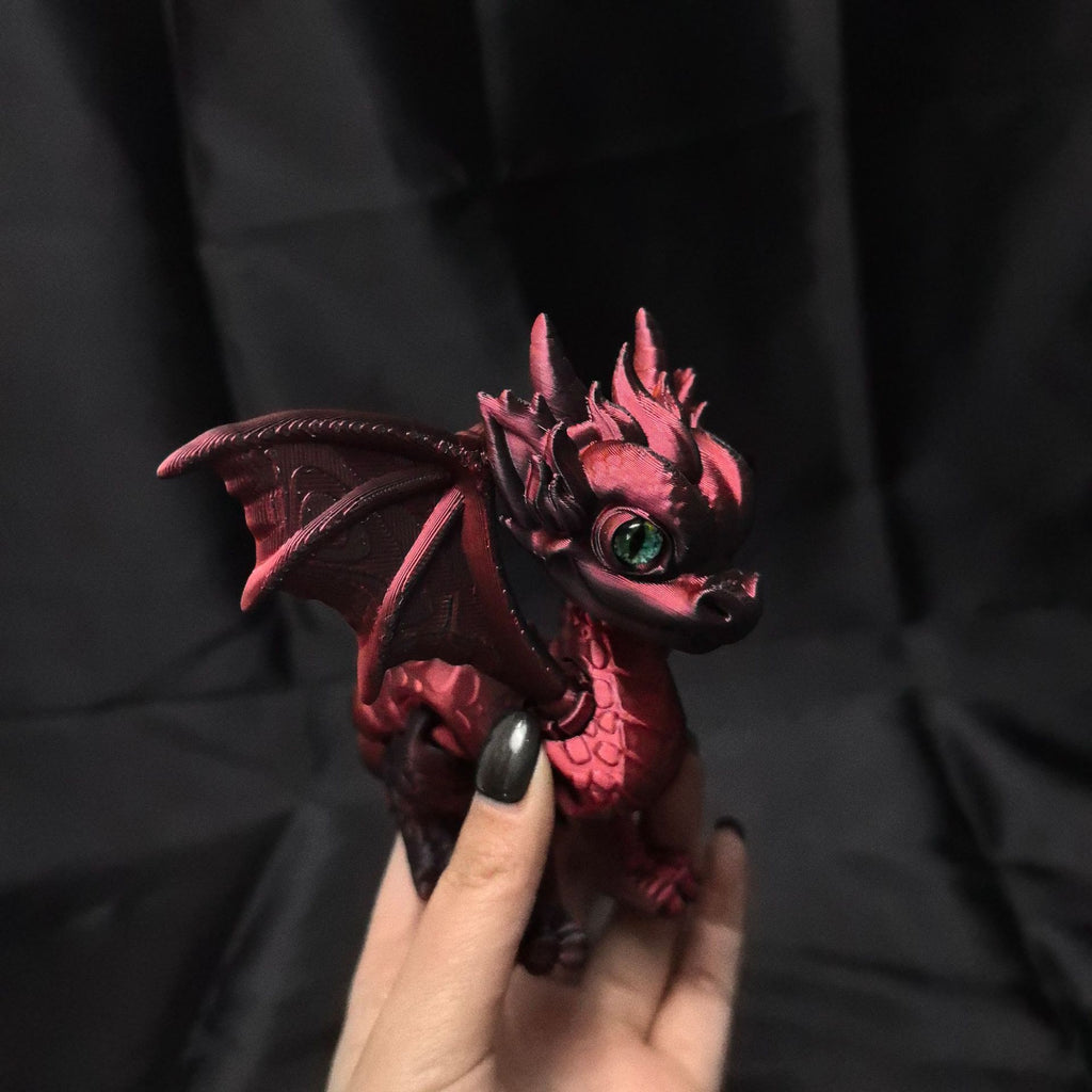 Dark red baby dragon figurine with green glass-look eye held in a hand for scale