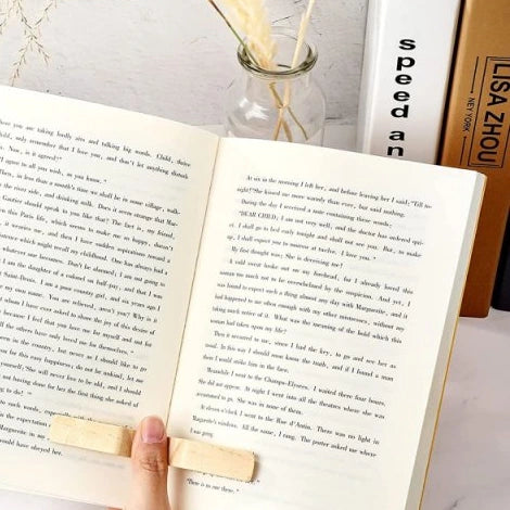The Page Warden wooden thumb page holder wedged into an open book, held in hand